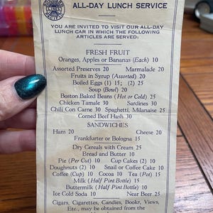 May include: A vintage beige paper menu titled ALL-DAY LUNCH SERVICE from Southern Pacific Lines. The menu lists various food items and prices, including fresh fruit, sandwiches, and beverages, with a circular logo at the top left corner.