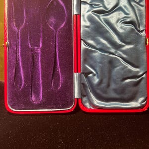 May include: Open red case with a purple velvet interior, featuring molded spaces for cutlery. The right side of the case is lined with blue satin. The case is open, revealing the interior design.