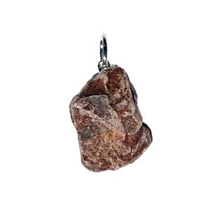 May include: A raw, unpolished reddish-brown stone pendant featuring a rough, textured surface with natural crystalline facets. The irregular, chunky mineral piece is securely attached to a small, polished silver-toned metal jump ring bail.