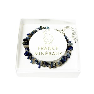 Puede incluir: Una pulsera hecha de fragmentos de piedra lapislázuli irregulares y pulidos en tonos azul profundo, gris y blanco. La pulsera cuenta con una cadena extensora de metal plateado y se presenta en una caja blanca con una tarjeta circular con el texto FRANCE MINÉRAUX.