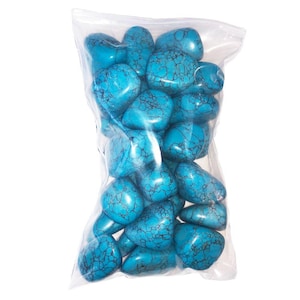 Puede incluir: Una bolsa de plástico transparente llena de varias piedras pulidas de color turquesa. Cada piedra presenta un patrón de matriz negro distintivo en forma de red sobre su superficie lisa y redondeada. Las piedras varían en tamaño y forma.