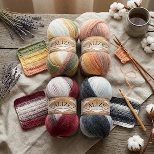 Peut inclure: Quatre pelotes de laine Alize Angora Gold aux dégradés variés, incluant jaune-vert, pêche-rose, rouge-bordeaux et bleu-gris. Chaque pelote porte une étiquette en papier. Des échantillons tricotés, des aiguilles en bois et un crochet sont présents.