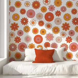 May include: A white couch with two white pillows and one orange pillow in front of a wall with a retro floral pattern. The pattern features orange, pink, and white flowers on a white background.