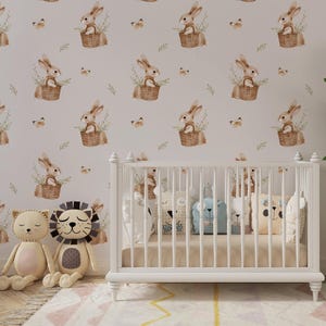 May include: A white wooden crib sits in front of wallpaper featuring a repeating pattern of brown bunnies in woven baskets, green sprigs, and small butterflies. Two plush animal toys, a cat and a lion, are positioned on the floor nearby.