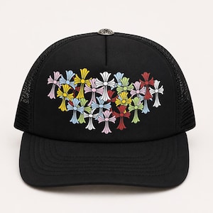 Könnte beinhalten: Eine schwarze Trucker-Cap mit Netzrückseite und festem Vorderteil. Auf der Vorderseite befindet sich eine Ansammlung von mehrfarbigen Kreuzgrafiken in Rot, Gelb, Hellblau, Rosa und Weiß. Ein kleiner silberfarbener Metallknopf befindet sich oben auf.