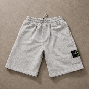 Könnte beinhalten: Hellgraue, melierte Jersey-Shorts mit elastischem Bund und Kordelzug. Die Shorts verfügen über eine seitliche Cargotasche, die mit einem schwarzen, rechteckigen Aufnäher mit einem gelb-grünen Kompass-Logo versehen ist.