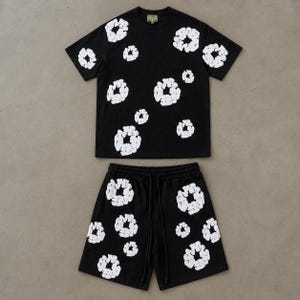 Könnte beinhalten: Ein Set aus einem schwarzen T-Shirt mit kurzen Ärmeln und passender Shorts, das mit einem sich wiederholenden weißen, kreisförmigen abstrakten Muster versehen ist. Das T-Shirt hat einen Rundhalsausschnitt und die Shorts einen Gummizug.