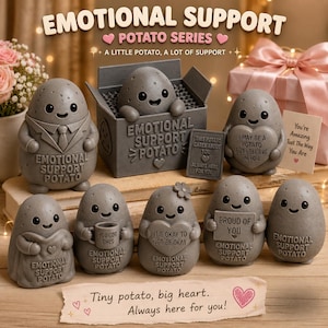 Peut inclure: Une collection de figurines en forme de pomme de terre grise avec des visages souriants et divers accessoires, incluant une boîte marquée Emotional Support Potato, un panneau indiquant This Potato Cares About You et une carte.