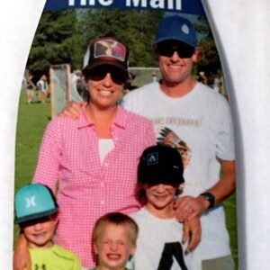 May include: A blue and white can cooler with the text "The Man" printed on the front. The cooler features a photo of a family of five, including two adults and three children. The adults are wearing hats, and the children are wearing various hats and shirts.