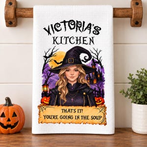 Peut inclure: Un torchon de cuisine blanc à tissage gaufré orné d'une sorcière aux cheveux blonds portant un chapeau noir. Le texte "VICTORIA'S KITCHEN" figure en haut et "THAT'S IT! YOU'RE GOING IN THE SOUP" en bas, sur un fond de maison hantée violette.