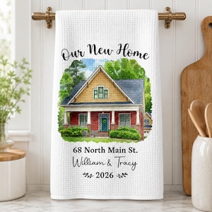 Pode incluir: Um pano de prato branco com textura de waffle apresentando uma ilustração em aquarela de uma casa com tijolos vermelhos e revestimento amarelo. O texto diz Our New Home, 68 North Main St., William & Tracy e 2026, em fontes pretas.