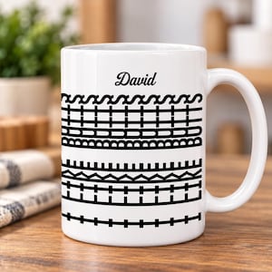 Puede incluir: Una taza de cerámica blanca con el nombre David en letra cursiva negra en la parte superior, seguido de varias filas horizontales de patrones geométricos negros y el texto vertical "BUTTS LIKE" integrado en el diseño a la derecha.