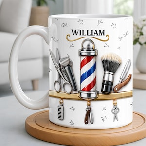 Puede incluir: Una taza de cerámica blanca con el nombre WILLIAM en texto negro sobre un gráfico central de poste de barbero. El diseño incluye ilustraciones de tijeras plateadas, una brocha de afeitar, una navaja y un peine sobre un fondo claro.