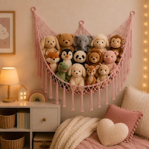 May include: A pink macrame wall-mounted hammock filled with a collection of plush stuffed animals, including a bear, elephant, monkey, panda, lion, pig, fox, deer, and various dogs, featuring long decorative fringe tassels hanging from the bottom.