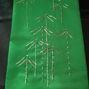 May include: A rectangular green fabric with an embroidered bamboo design. The bamboo stalks and leaves are crafted with silver and gold-colored beads, creating a textured, decorative pattern. The fabric has a subtle sheen.