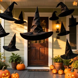 May include: Multiple black pointed witch hats suspended in the air at varying heights. Below the hats, several orange pumpkins with carved jack-o'-lantern faces are arranged on a porch floor, accompanied by potted green plants near a wooden door.