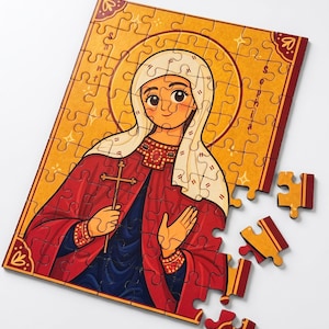 Può includere: Un puzzle rettangolare con un'illustrazione stilizzata di una figura con aureola, che indossa un copricapo bianco e una veste rossa sopra un indumento blu scuro, mentre tiene in mano una croce. Il testo "Saint Sophia" è scritto verticalmente a destra.