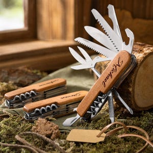 May include: Three multi-tools with wooden handles, each engraved with a name: Michael, Steven, and Aaron. One tool is open, displaying multiple stainless steel blades, a saw, scissors, and a bottle opener. The handles have a smooth, light brown finish.
