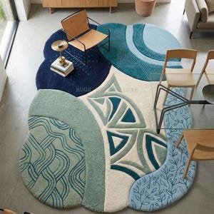 Könnte beinhalten: Ein unregelmäßig geformter Teppich mit einem strukturierten Design in Marineblau, Petrol, Salbeigrün und Creme. Der Teppich zeigt verschiedene Muster, darunter geometrische Dreiecke, wellenförmige Linien und botanische Motive mit dem Text RUGS LUXE.