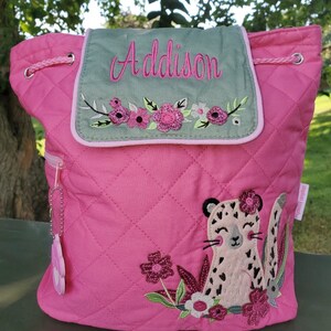 May include: Pink quilted backpack with a green flap featuring the name "Addison" embroidered in white. The flap has a floral design with pink, white, and green flowers. The backpack also features a pink embroidered cheetah with black spots and a floral design.