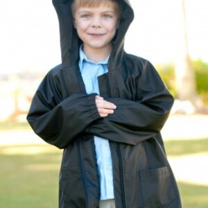 May include: A black hooded rain jacket with a front zipper closure, long sleeves with elastic cuffs, and two front patch pockets. The jacket is worn over a light blue button-down shirt and light-colored trousers.