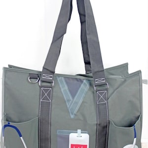 May include: A green canvas tote bag with a doctor's scrubs design. The bag has two large pockets on the front, a smaller pocket with a stethoscope, and a pocket with a heart rate monitor. The bag has two black straps.
