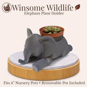 May include: A gray elephant plant holder with a small succulent in a brown pot. The holder is on a round wooden base with a marble top. The text "Winsome Wildlife Elephant Plant Holder" is at the top. Fits 4" nursery pots.