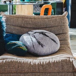 May include: A brown upholstered lounge chair with decorative cushions. The cushions include a large grey, oval-shaped cushion with black linear designs, and two smaller, round cushions in blue and teal.