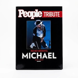 May include: A black hardcover book titled People Tribute Remembering Michael 1958-2009. The cover features a central photograph of a performer wearing a black hat, white shirt, black jacket, and a white glove, standing on a stage with a microphone.