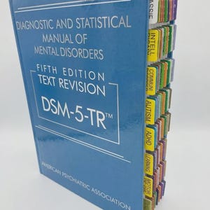May include: A blue hardcover book titled Diagnostic and Statistical Manual of Mental Disorders Fifth Edition Text Revision DSM-5-TR by the American Psychiatric Association, featuring a series of colorful index tabs along the side edge.