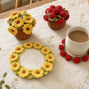 Könnte beinhalten: Zwei gehäkelte Blumentöpfe mit gelben und roten Blüten sowie zwei runde gehäkelte Untersetzer mit gelben und roten Blumenrändern. Auf einem Untersetzer steht eine weiße Keramiktasse, die mit einem hellbraunen Getränk gefüllt ist.