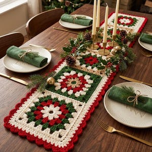 Op de afbeelding: Een rechthoekige gehaakte tafelloper met een herhalend granny square patroon in rood, donkergroen en crèmekleurig garen. De loper heeft een geschulpte rode rand en is versierd met vier hoge crèmekleurige dinerkaarsen in gouden houders en dennentakken.