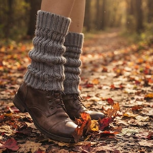 May include: A pair of grey knitted leg warmers with a ribbed texture worn over dark brown leather lace-up boots. The leg warmers extend from the ankle to the mid-calf, featuring a thick, chunky knit pattern that provides a layered appearance.