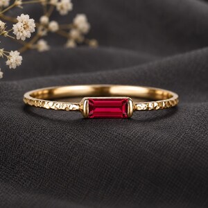Op de afbeelding: Een gouden ring met een horizontaal geplaatste, in baguette geslepen rode edelsteen in het midden. De ringband heeft een opvallende gehamerde textuur, wat zorgt voor een reflecterende en onregelmatige afwerking van het oppervlak.