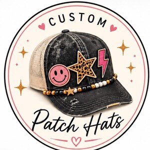 Puede incluir: Una gorra de camionero negra con efecto desgastado y parte trasera de malla, decorada con un parche de cara sonriente rosa, una estrella con estampado de leopardo y un rayo rosa. Un borde de cuentas negras, doradas y blancas rodea la base. Texto: CUSTOM Patch Hats.
