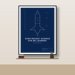 May include: A framed dark blue poster featuring a white line drawing of a rocket blueprint. The text reads: EVEN ROCKET SCIENCE CAN BE LEARNED. So is everything else. The design includes technical labels for payload and stages in a schematic style.