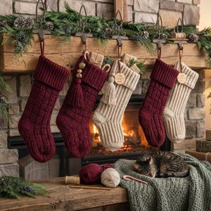 May include: Five knitted Christmas stockings in alternating burgundy and cream colors hang from a wooden mantel. The stockings feature ribbed cuffs and textured patterns. Two stockings have decorative tassels and wooden tags with text.