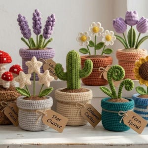 May include: A collection of eight crocheted potted plants including red mushrooms, purple lavender, white daisies, purple tulips, cream stars, a green cactus, a green fern spiral, and a yellow sunflower, each with a brown paper tag.