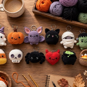 May include: A collection of twelve small crocheted Halloween-themed keychains including a ghost, pumpkin, bat, black cat, mummy, Frankenstein monster, candy corn, skull, spider, red heart, cauldron, and a small basket filled with candy corn pieces.