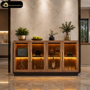 May include: A wooden sideboard with four glass-fronted doors and internal warm LED lighting. The cabinet features gold vertical handles and contains various glassware, bottles, and decorative items. Three potted plants sit on the top surface.