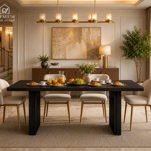 May include: A rectangular black dining table with a fluted base and four cream-colored upholstered chairs with gold metal legs. The table is set with white plates, glasses of orange juice, croissants, and a bowl of green grapes in the center.