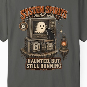 Könnte beinhalten: Ein dunkelgraues T-Shirt mit einer Grafik eines alten Fernsehers, der einen Geist zeigt, dazu eine schwarze Katze und elektrische Geräte. Der Text lautet SYSTEM SPIRITS control room und HAUNTED, BUT STILL RUNNING, mit einer kleinen Laterne.