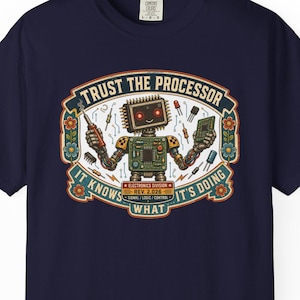May include: A navy blue t-shirt featuring a graphic of a robot holding electronic components. The text reads TRUST THE PROCESSOR IT KNOWS WHAT IT'S DOING, ELECTRONICS DIVISION REV. 2.026, SIGNAL, LOVE, CONTROL. The design is framed by floral motifs.