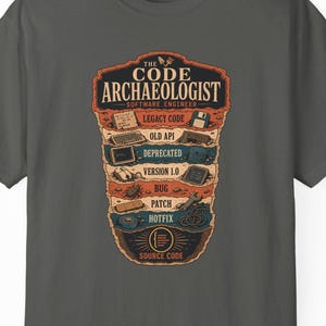 Könnte beinhalten: Ein anthrazitfarbenes Kurzarm-T-Shirt mit einem Grafikdruck mit der Aufschrift The Code Archaeologist Software Engineer. Das Design zeigt gestapelte Schichten der Computergeschichte, darunter legacy code, old API, deprecated, version 1.0, bug, patch, hotfix und source code.