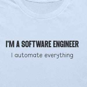 May include: A light blue t-shirt featuring the black text I'M A SOFTWARE ENGINEER and I automate everything printed on the front. The shirt is displayed alongside a straw hat, two small potted succulents, brown sunglasses, and blue denim jeans.