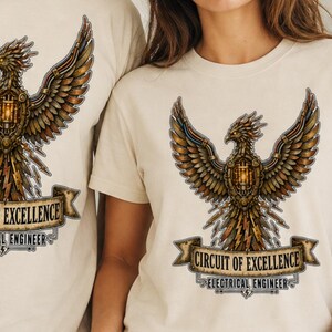 May include: A cream-coloured short-sleeve t-shirt featuring a graphic of a mechanical phoenix with spread wings. Below the bird is a banner with the text "CIRCUIT OF EXCELLENCE" and "ELECTRICAL ENGINEER" printed in a dark, stylised font.