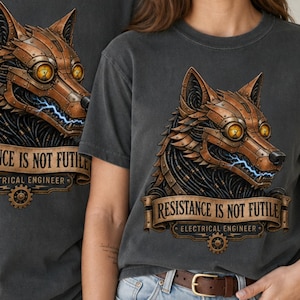 Può includere: Una t-shirt grigio antracite a girocollo con la grafica di un lupo meccanico dagli occhi gialli luminosi e scintille elettriche blu. Sotto il lupo, un nastro riporta il testo "RESISTANCE IS NOT FUTILE" e "ELECTRICAL ENGINEER."
