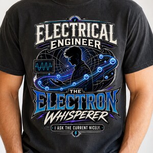 May include: A charcoal gray t-shirt featuring a graphic print with the text "ELECTRICAL ENGINEER THE ELECTRON WHISPERER I ASK THE CURRENT NICELY." The design includes a silhouette of a person, blue electrical waves, and circuit symbols.