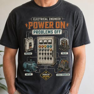 Könnte beinhalten: Ein anthrazitfarbenes T-Shirt mit einem Grafikdruck und dem Text "ELECTRICAL ENGINEER POWER ON PROBLEMS OFF". Das Design zeigt Illustrationen eines Schutzschalters, eines Bedienfelds, eines Relais, eines Motors und Kabelanschlüssen.