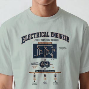 Könnte beinhalten: Ein helles salbeigrünes T-Shirt mit einer dunkelblauen und orangefarbenen Grafik eines elektrotechnischen Schaltplans. Der Text lautet ELECTRICAL ENGINEER, POWER PROTECTION PRECISION, RING MAIN UNIT, DISTRIBUTION TRANSFORMER und LOW VOLTAGE SWITCHBOARD.